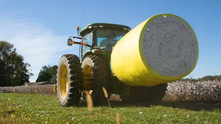 A green tractor transports a bale of cotton